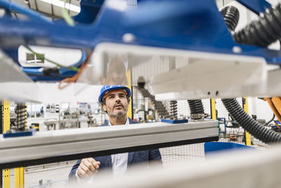 Thoughtful engineer looking at machine parts in factory