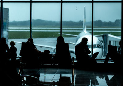 Silhouette people sitting at airport window