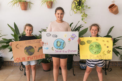 Smiling girls with posters standing at home