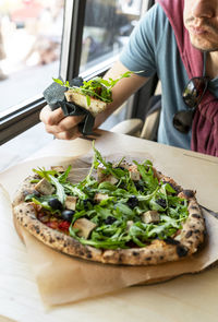 Man eating vegan pizza with arugula or rucola tofu olives and tomatoes vegetarian food healthy 