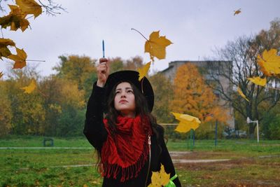 Young woman standing with leaves in mid-air on field during autumn