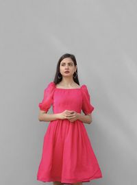 Portrait of young woman standing against gray background