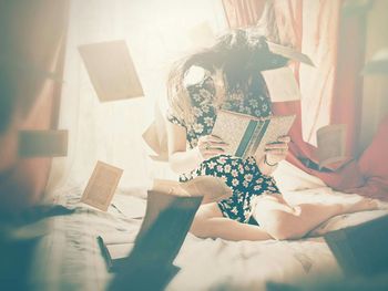 Girl reading book on bed while papers are flying around her