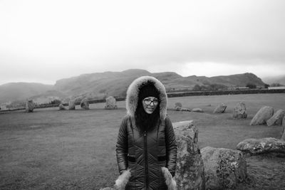 Portrait of young woman standing on field against sky