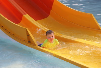 Portrait of boy on yellow slide in swimming pool