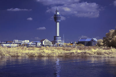 Lighthouse by lake and buildings against sky