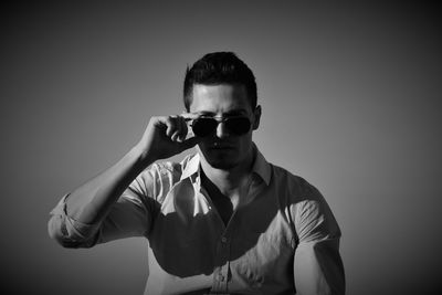 Young man holding sunglasses against gray background