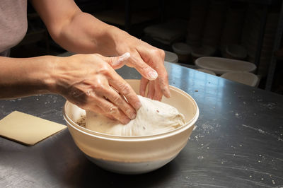 Of a baker's female hands dipping dough into a bowl of seeds and cereals before baking artisan bread