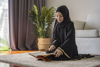 Young woman reading koran while sitting on floor at home