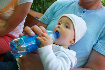 Close-up of baby girl holding bottle while lying on father