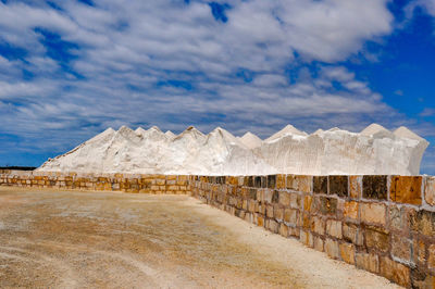 View of wall and salt hill against cloudy sky