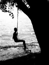 Silhouette of boy on swing at sea