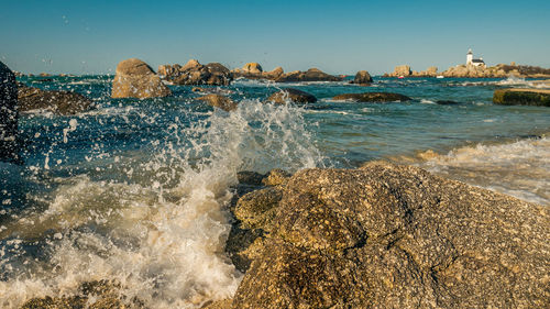 Sea waves splashing on rocks against clear sky