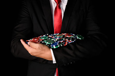 Midsection of businessman holding gambling chips against black background