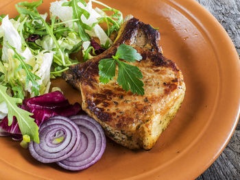 Close-up of roasted pork chop with salad in plate on table