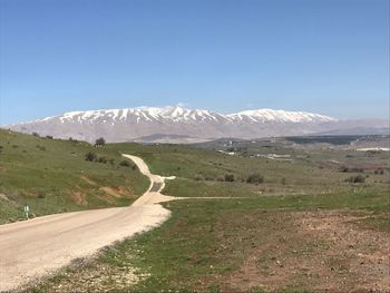 Road leading towards mountains against clear blue sky