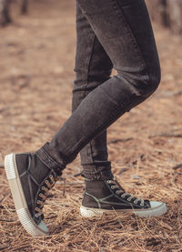 Female legs in stylish jeans and sneakers in a pine forest