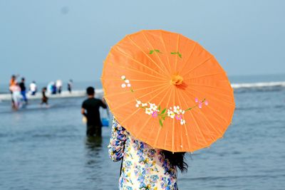 Rear view of woman with orange umbrella standing at beach