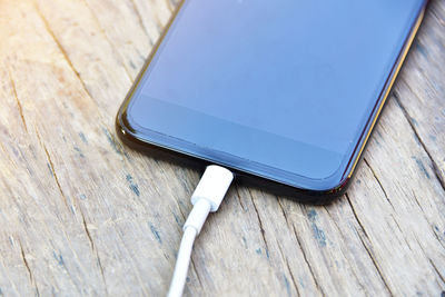 Close-up of usb cable connected to mobile phone on wooden table