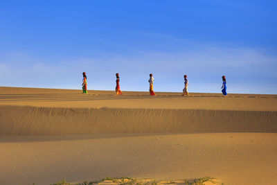 People on sand dune in desert against sky