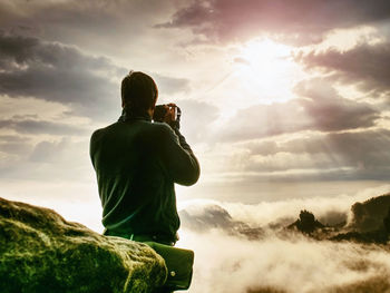 Photographer on cliff with camera viewfinder at his face. nature photographer takes photos  of fog