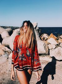 Young woman on rock at beach against sky