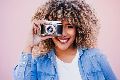 Portrait of young woman with camera against wall