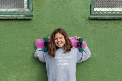 Portrait of smiling young woman standing against wall