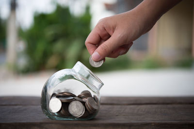 Close-up of person putting coin in jar on table