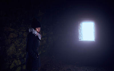 Woman standing against wall in dark room