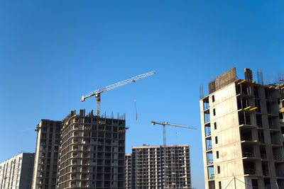 Low angle view of crane and buildings against clear blue sky