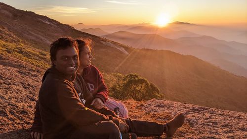 Side view of woman sitting on mountain against sky during sunset