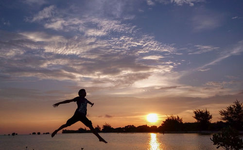 Silhouette man by lake against sky during sunset