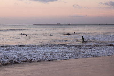 People enjoying in sea against sky during sunset