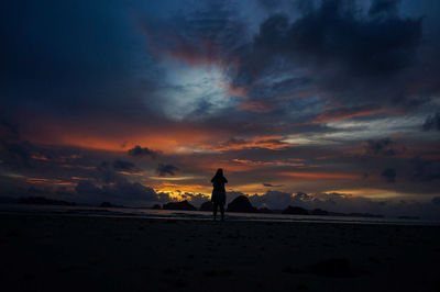 Silhouette man walking on snow covered landscape against sky during sunset