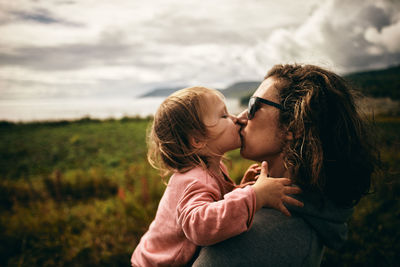Side view of mother kissing daughter while standing on land