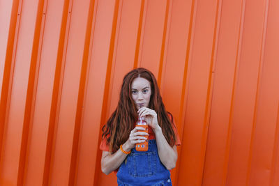 Portrait of woman standing against orange wall