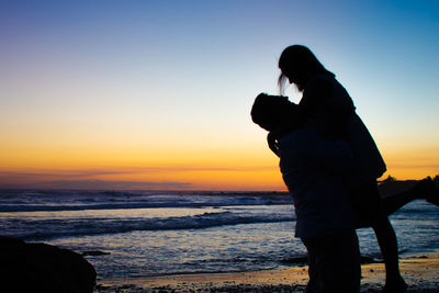 Silhouette couple photographing sea against sky during sunset