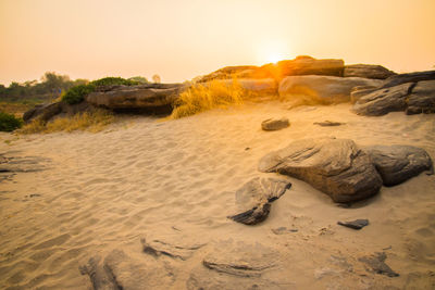 Rocks on beach against sky during sunset