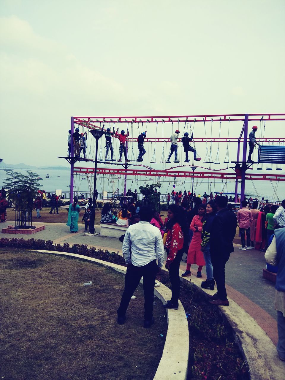 REAR VIEW OF PEOPLE WALKING ON BRIDGE AGAINST SKY IN CITY