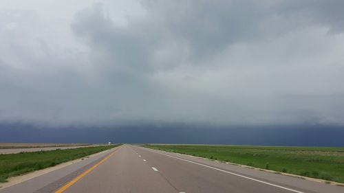 Road passing through field against cloudy sky