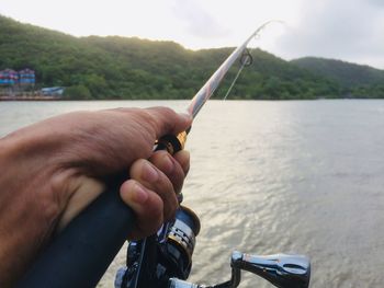 Close-up of hand holding fishing rod over river