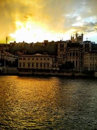 Buildings by river against sky during sunset