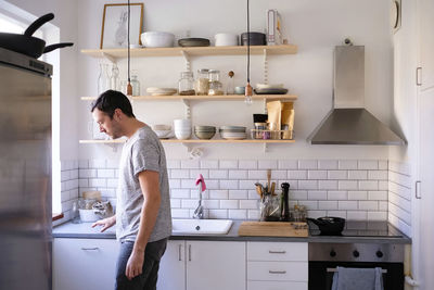 Side view of man standing by kitchen counter at home