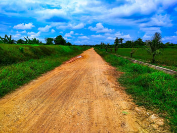 Dirt road amidst field against sky