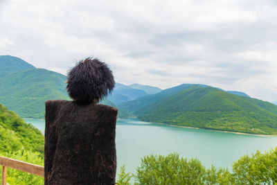 Rear view of man overlooking calm sea against mountain range