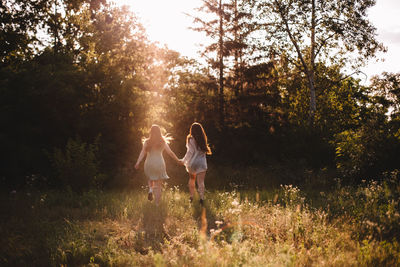 Back view of girlfriends holding hands while running in summer forest