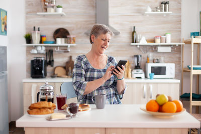 Senior woman holding mobile phone at kitchen