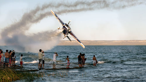 People standing by crashing air vehicle on shore against sky