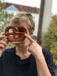 Close-up portrait of mature woman holding pretzel while standing outdoors